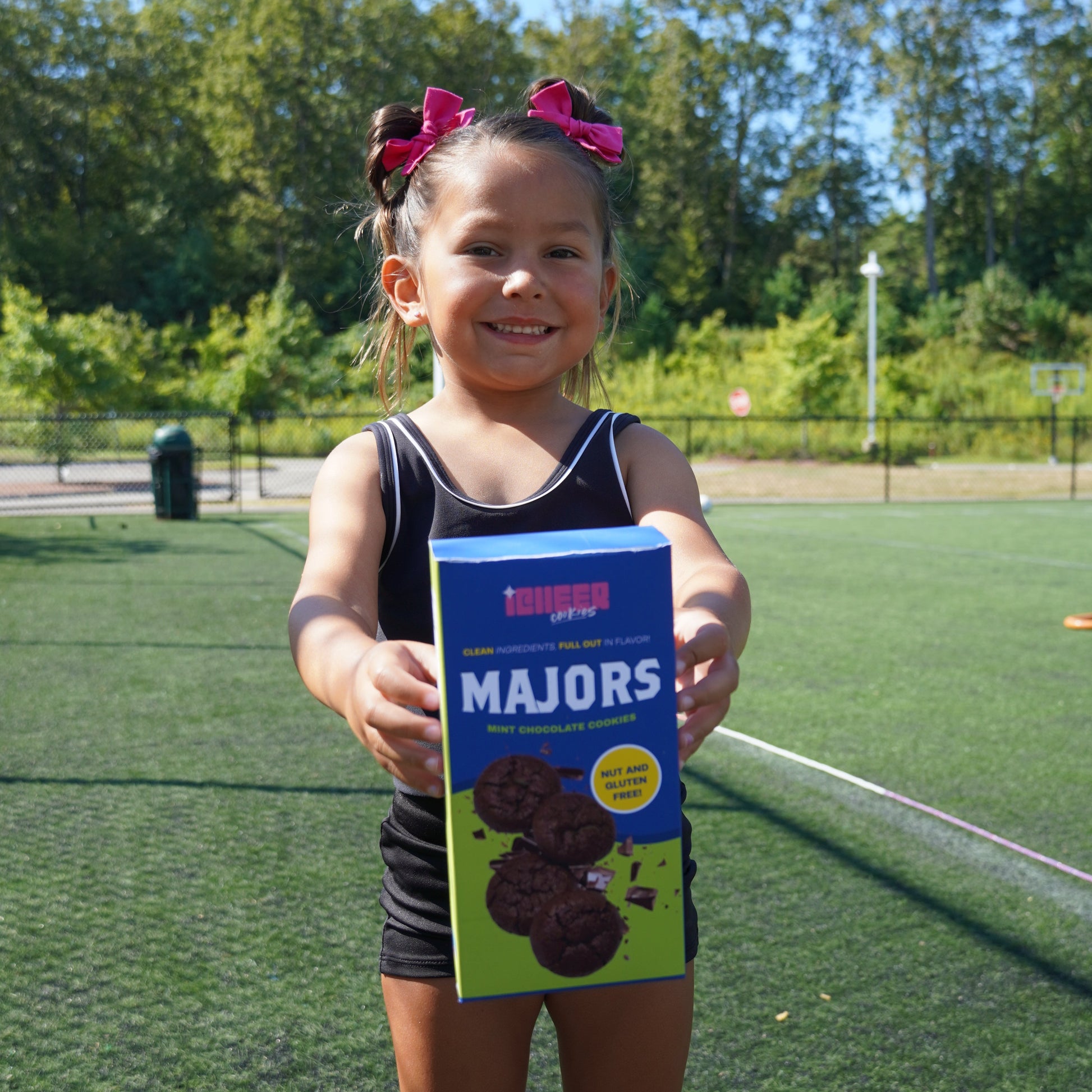Person holding a box of Majors cookies on a grassy field with trees and a clear sky.